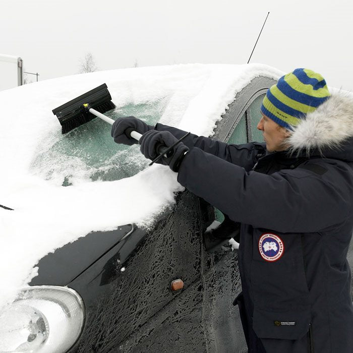 Man die sneeuw van de voorruit van een auto krabt