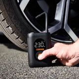 Hånd trykker på tænd/sluk-knap på Osram TYREinflate 1600 ved bildæk, display viser 230 kPa