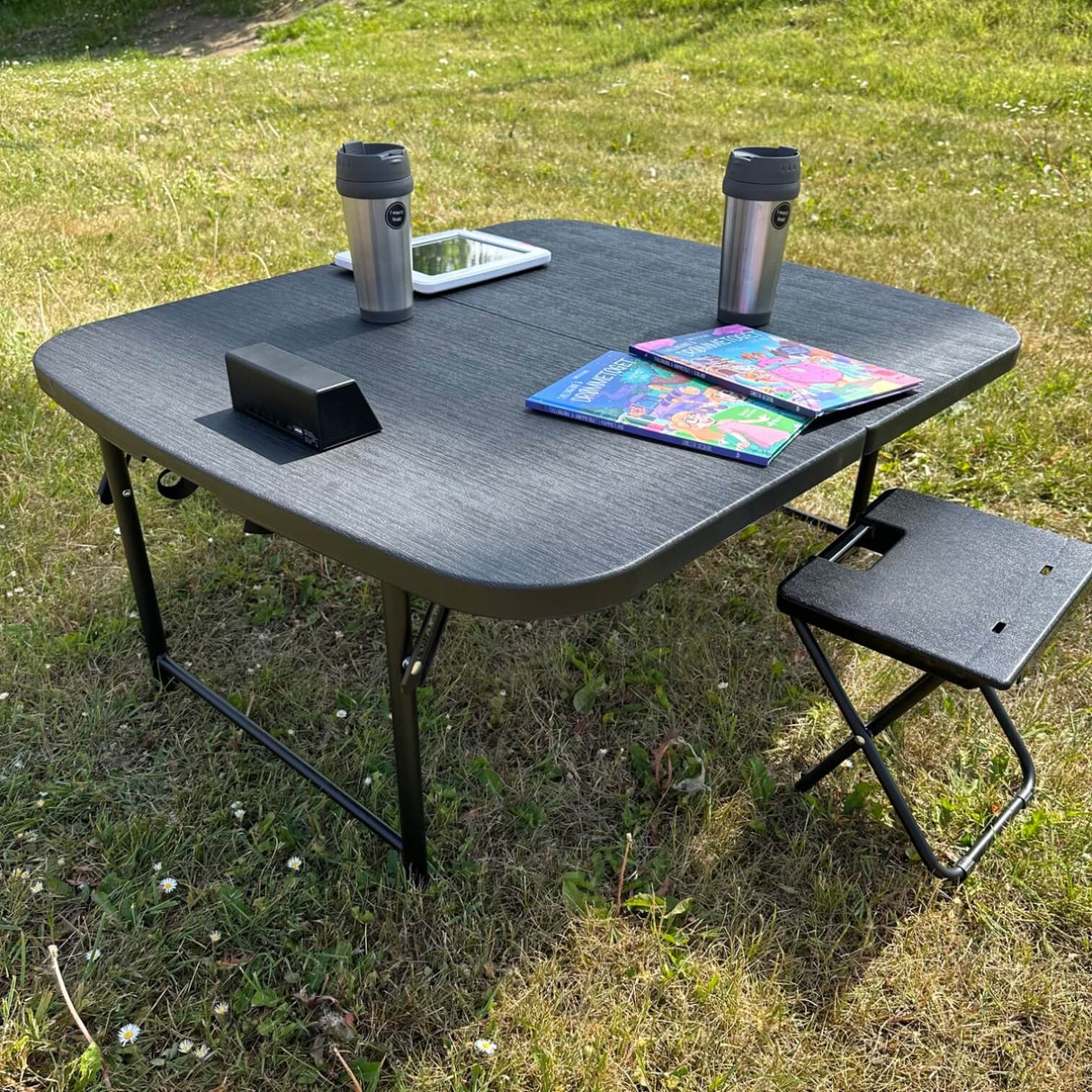 zwarte campingtafel met koffiekopje, kinderboeken en een tablet