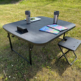 zwarte campingtafel met koffiekopje, kinderboeken en een tablet