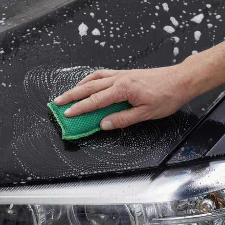 Hand wast auto met groene spons en zeepbellen.