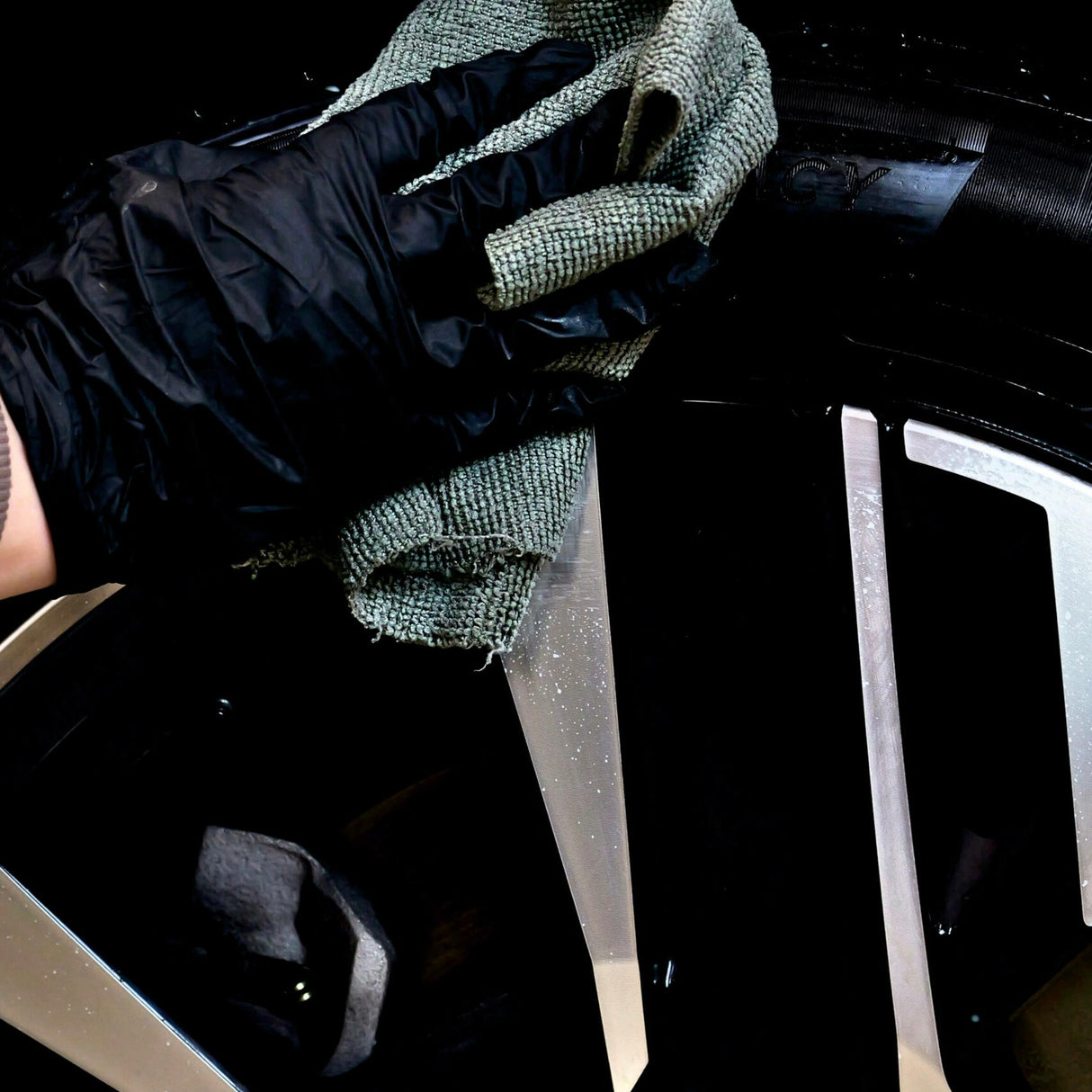 Hand met handschoen brengt Autoland bandenwax aan op een autoband met een doek.