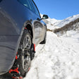 Sneeuwkettingen gemonteerd op een grijze autoband in besneeuwde bergen