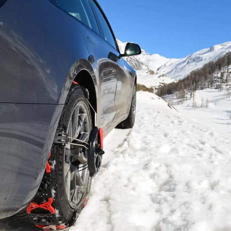 Sneeuwkettingen gemonteerd op een grijze autoband in besneeuwde bergen