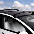 Tesla Model Y met zwarte dakdragers onder een blauwe lucht met wolken
